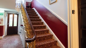A grand staircase with ornate railings, a red wall, and framed pictures. - City Studios - Rodney Street (Liverpool)