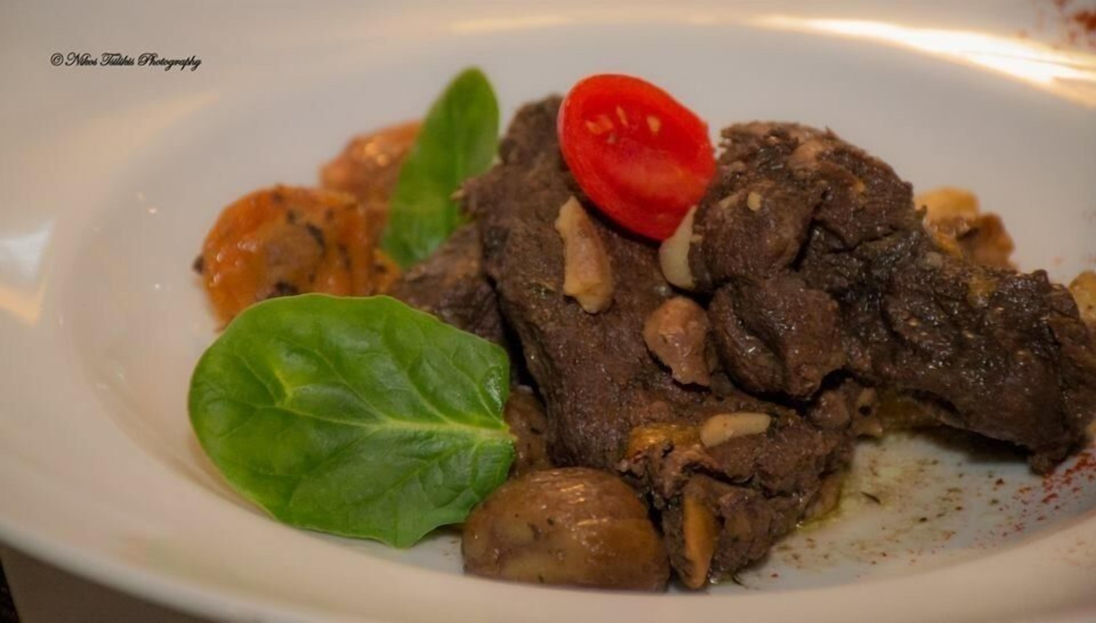 Une assiette contenant de la viande en tranches, des champignons et une tomate cerise.