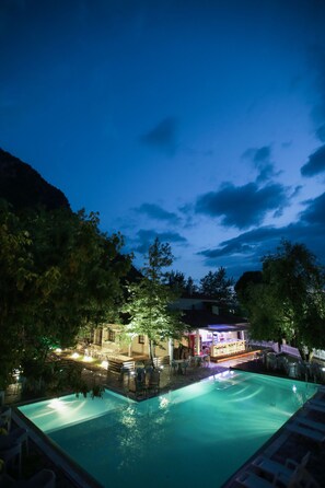 Vista nocturna de un área de piscina con bar y sillones de descanso.