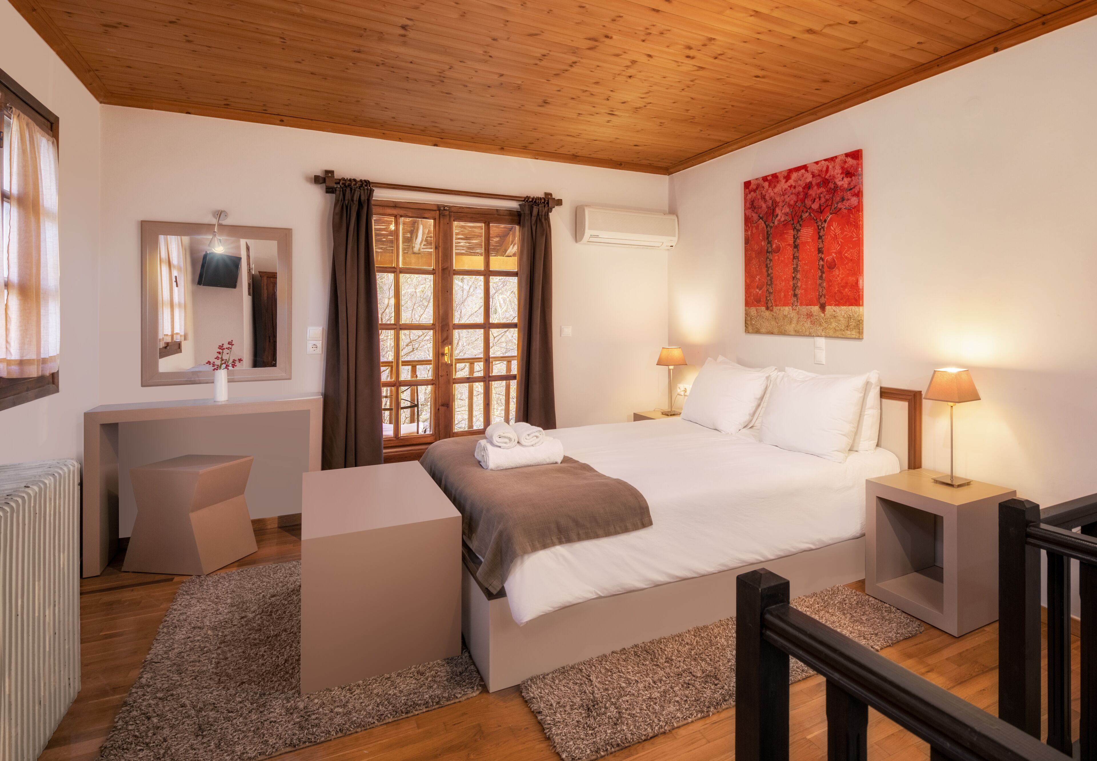 Un dormitorio con cama, mesitas de noche, escritorio, espejo y ventana con cortinas.