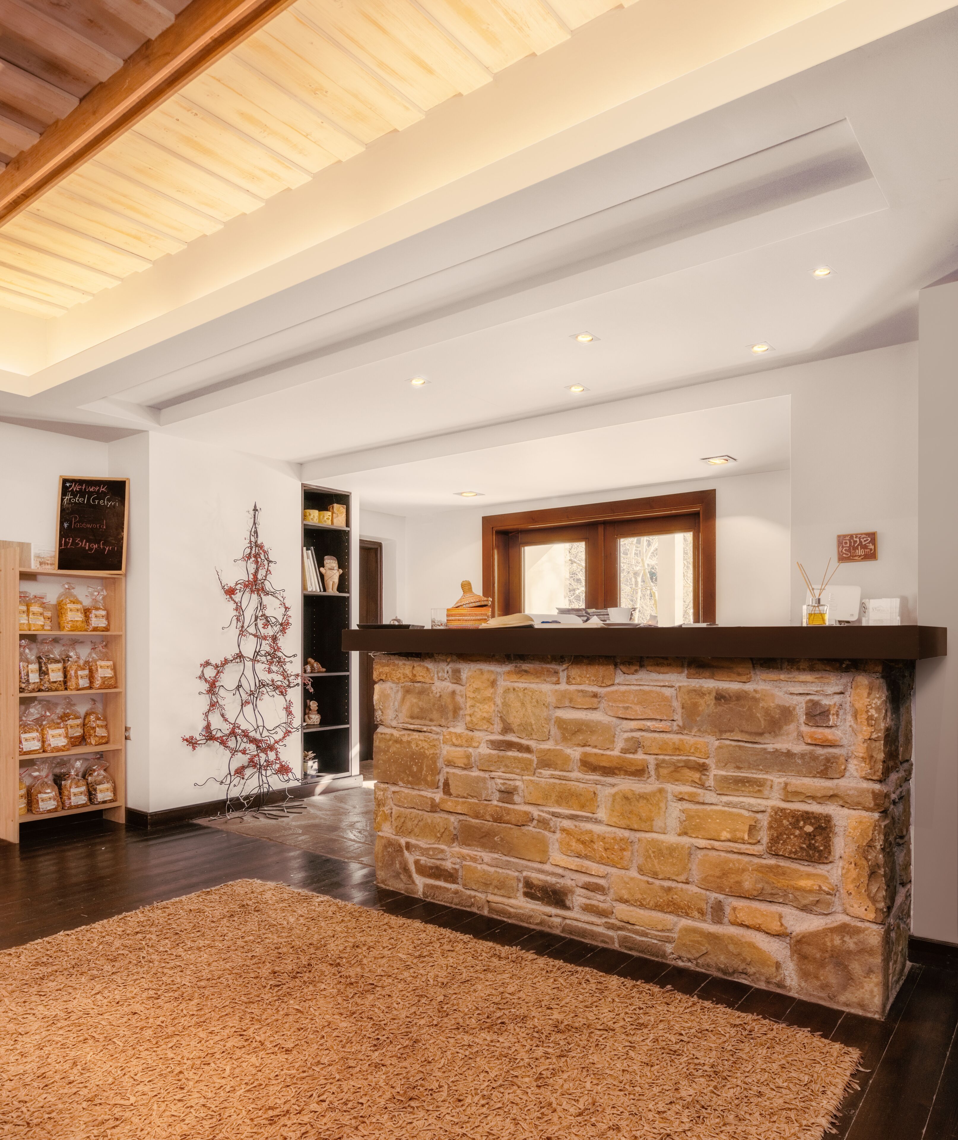 A reception area with a stone counter, wooden shelves with products, a decorative tree, and a view through a doorway.