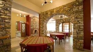A restaurant with stone walls, round tables with red tablecloths, and a fireplace. - Lydia Hotel (Kavala)