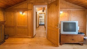 A wooden interior with a television on a wooden stand, a hallway leading to another room, and wooden walls with built-in lighting. - B&B Marie Thérèse (Torreano)