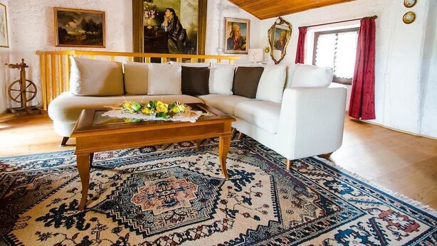 A cozy living room with a wooden ceiling, a white sofa, a wooden coffee table, and a patterned rug. - B&B Marie Thérèse (Torreano)