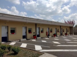 Une rangée de chambres d’hôtel avec des portes num érotées, un parking avec des flèches indiquant le sens de circulation et des plantes en pot.