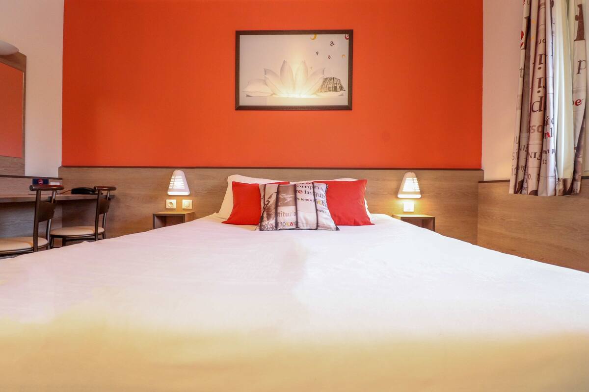 A hotel room with a large bed, two bedside lamps, a desk with a chair, and a framed picture on the wall.