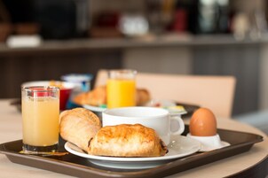 Un plateau de petit-déjeuner avec des croissants, un verre de jus d’orange, une tasse de café et une assiette contenant un œuf à la coque.