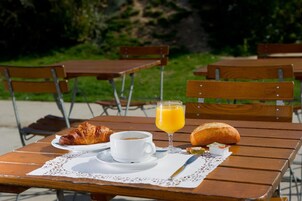 Une table en bois avec un croissant, une tasse de café et un verre de jus d’orange.