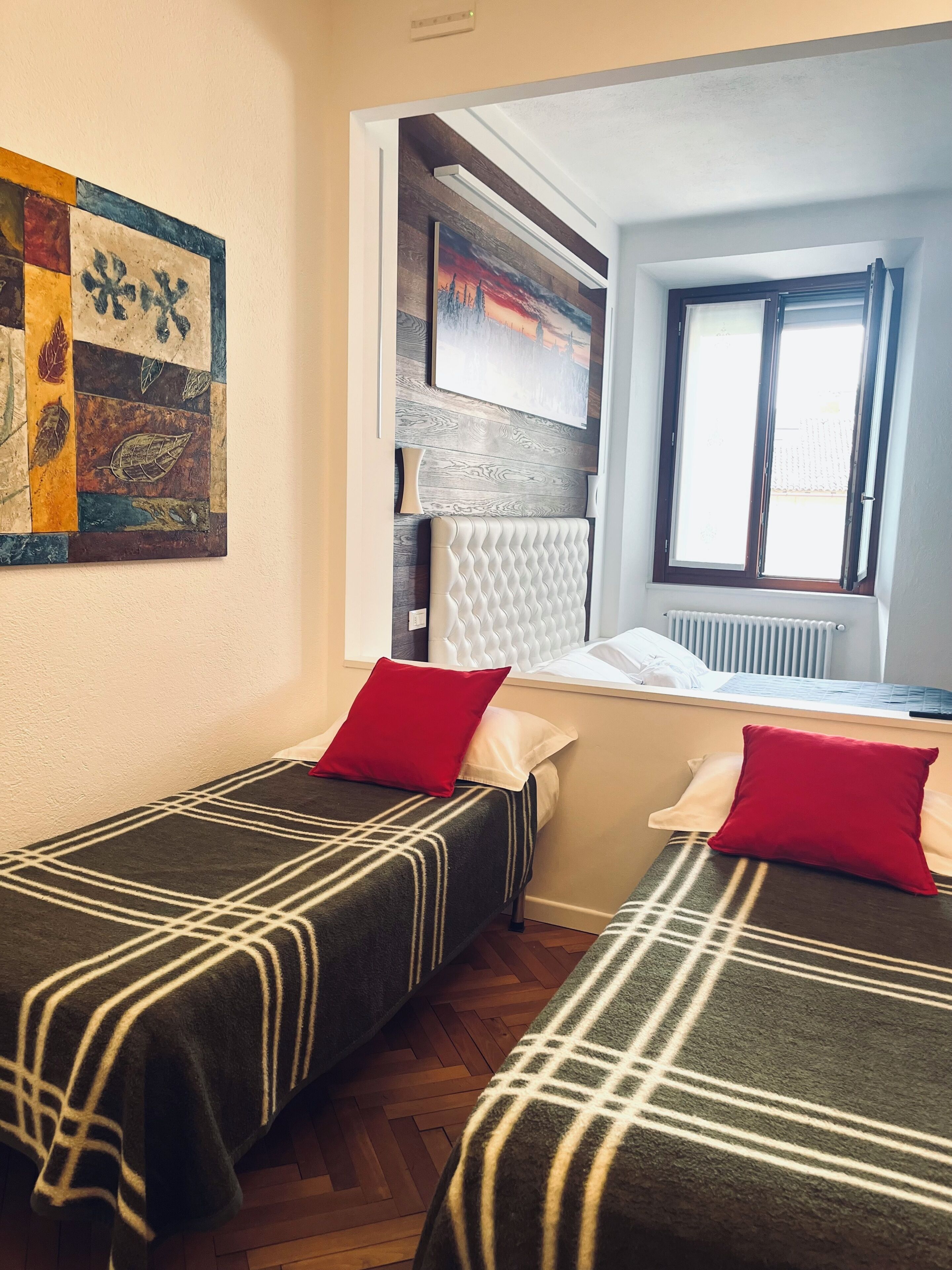 A room with two beds, a window, a radiator, and a painting on the wall.