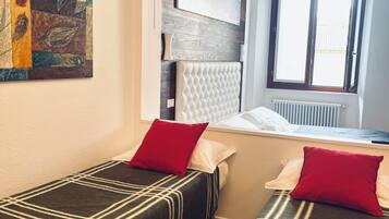 A room with two beds, a window, a radiator, and a painting on the wall.