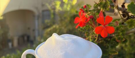 A white cup of coffee with foam on a saucer, held by a hand.