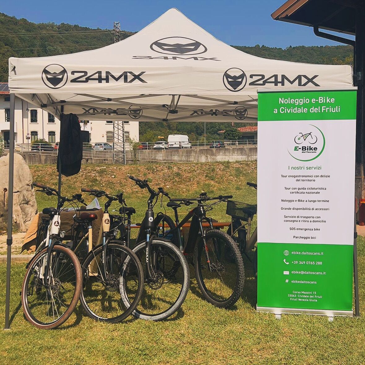 Una tienda de campaña con la marca '24MX' y un cartel que anuncia servicios de alquiler de bicicletas eléctricas.