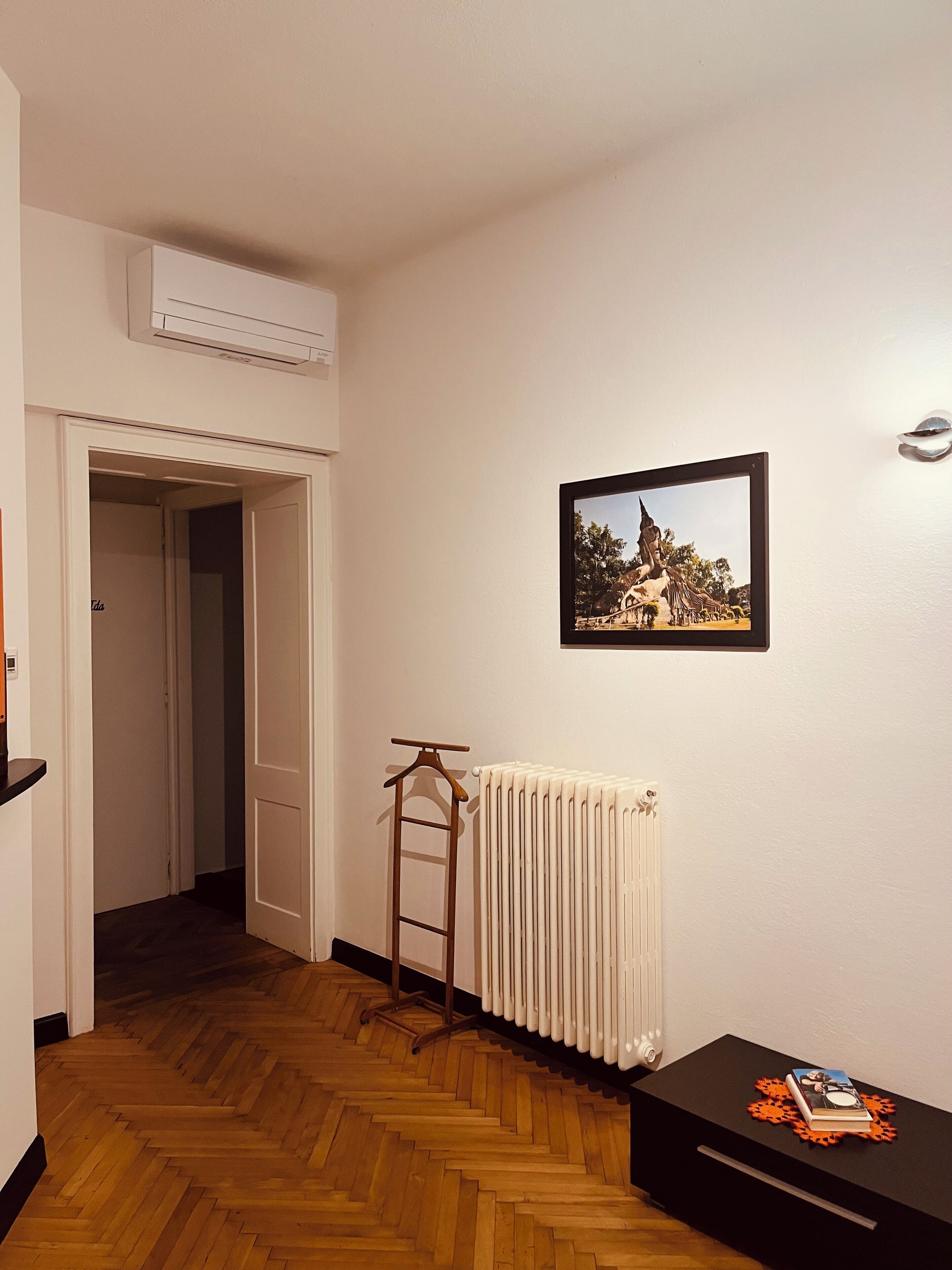 Um corredor com um radiador, um quadro emoldurado na parede e um cabide de madeira encostado no radiador.