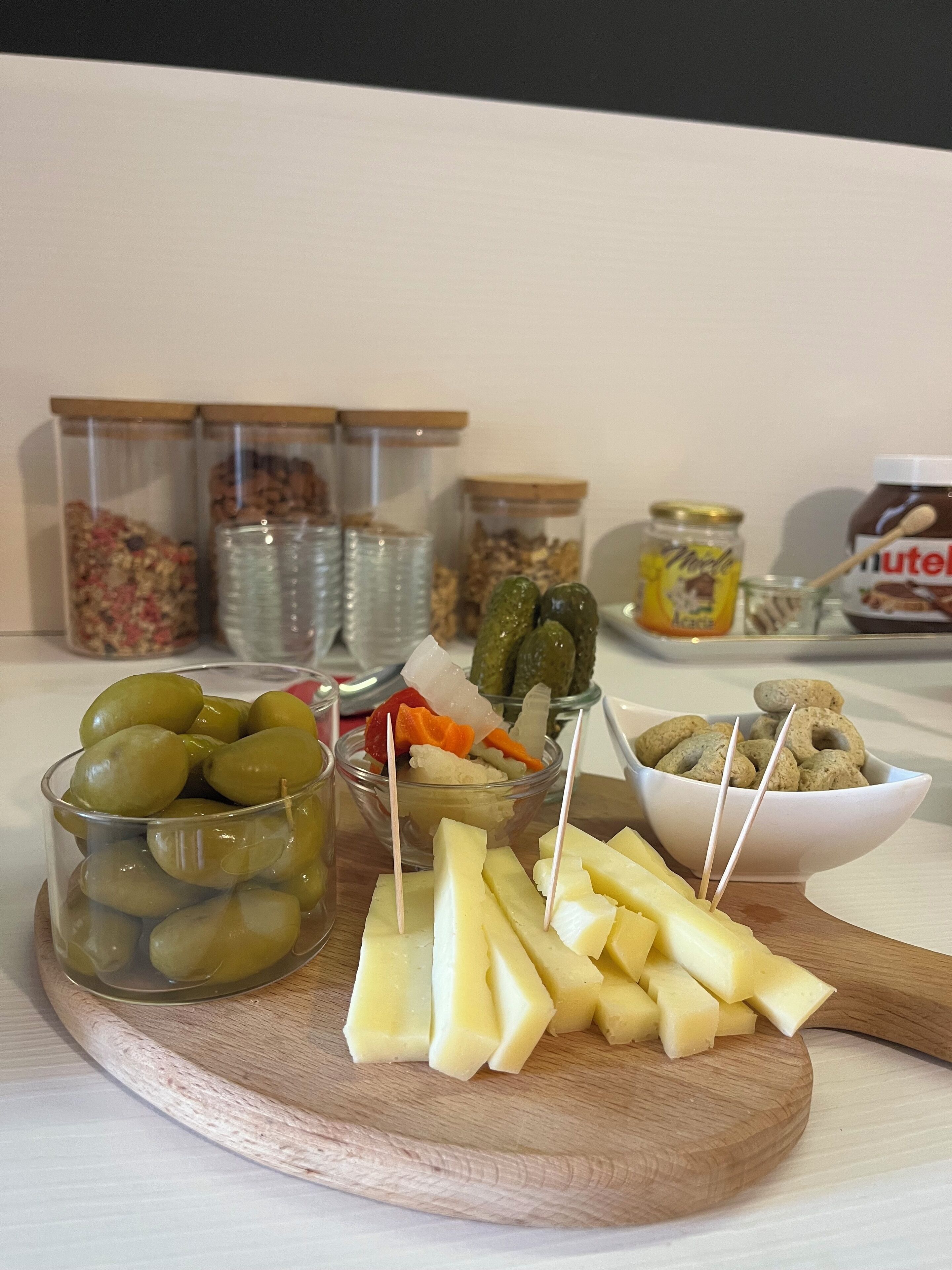 A wooden board with various food items including olives, pickles, cheese, and nuts.