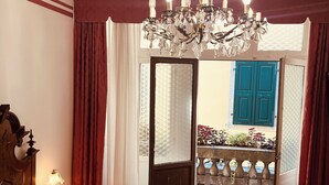 A bedroom with a large bed, a chandelier, and a view of a balcony with blue shutters.