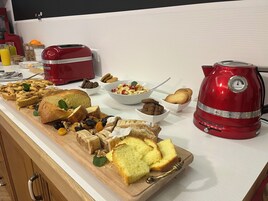 Una encimera de cocina con una variedad de productos horneados, incluyendo pan y pasteles, y una batidora roja KitchenAid.