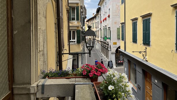A narrow street with buildings on either side, a street lamp, and flower boxes with various flowers.