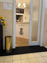 Zona de recepción con un letrero que dice 'dai Toscans', una lámpara de araña, un cubo de basura y una puerta que da a una habitación con piso de diseño espiga.