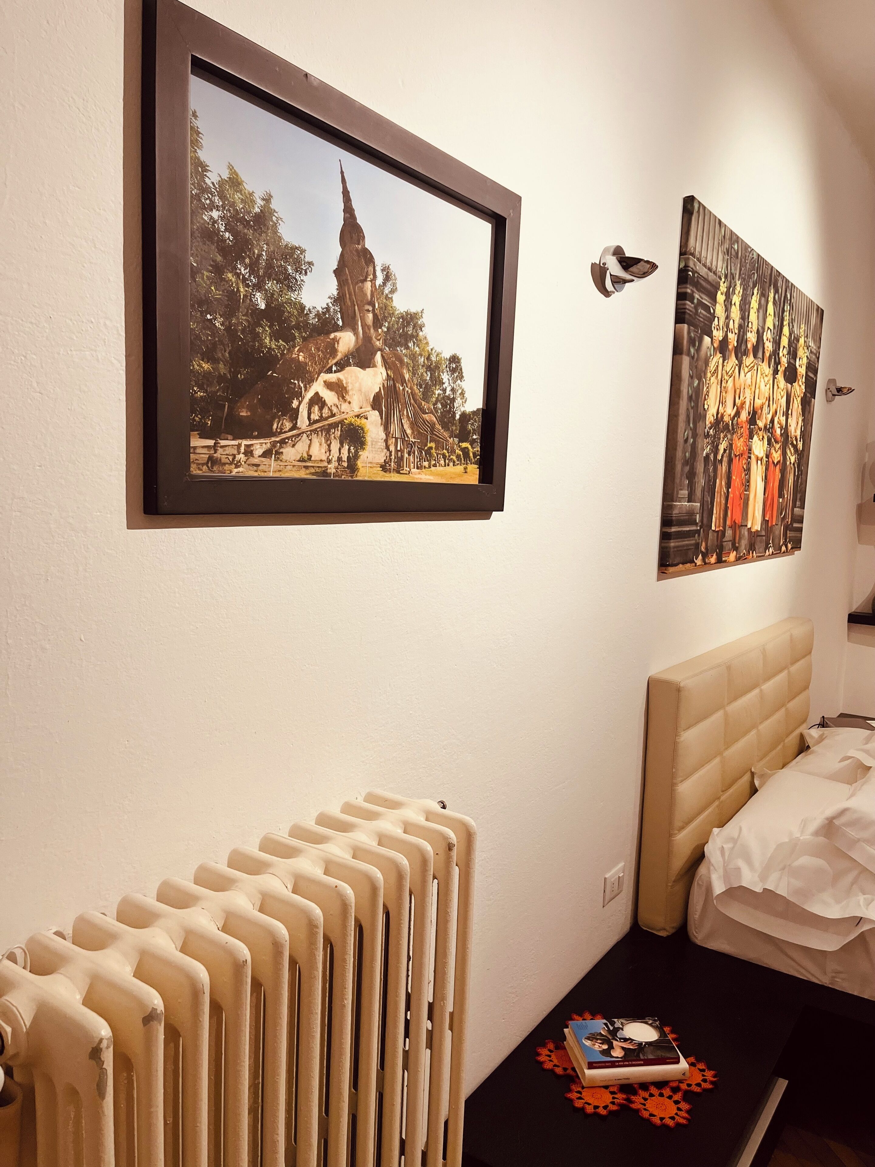Un dormitorio con radiador, una cama, un cuadro enmarcado de un templo y una lámpara fijada a la pared.