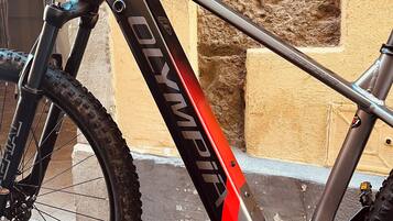 Una bicicleta con la marca "Olympia", horquilla delantera con suspensión y desviador trasero.