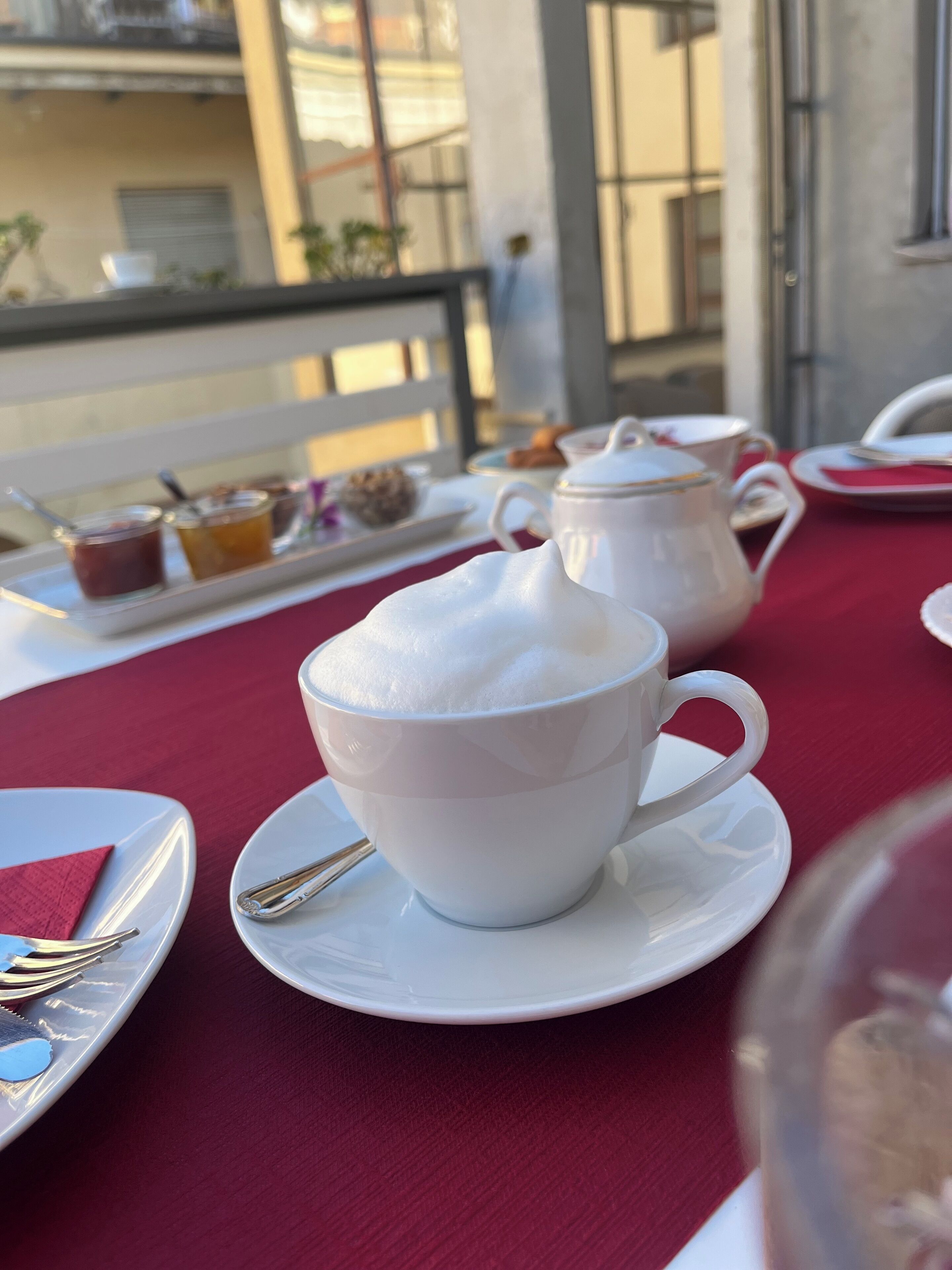 Una mesa con una taza blanca de café y una tetera sobre un mantel rojo.