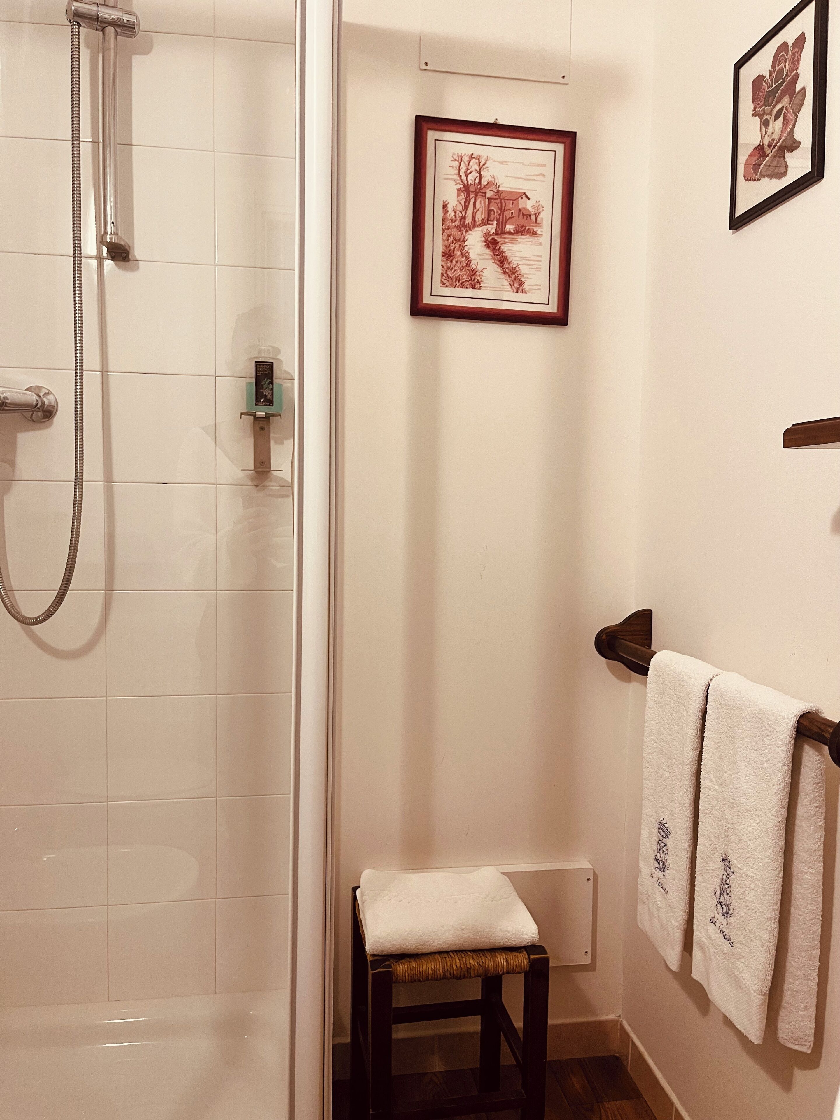 A bathroom with a shower, a small stool, and two towels hanging on a rack.