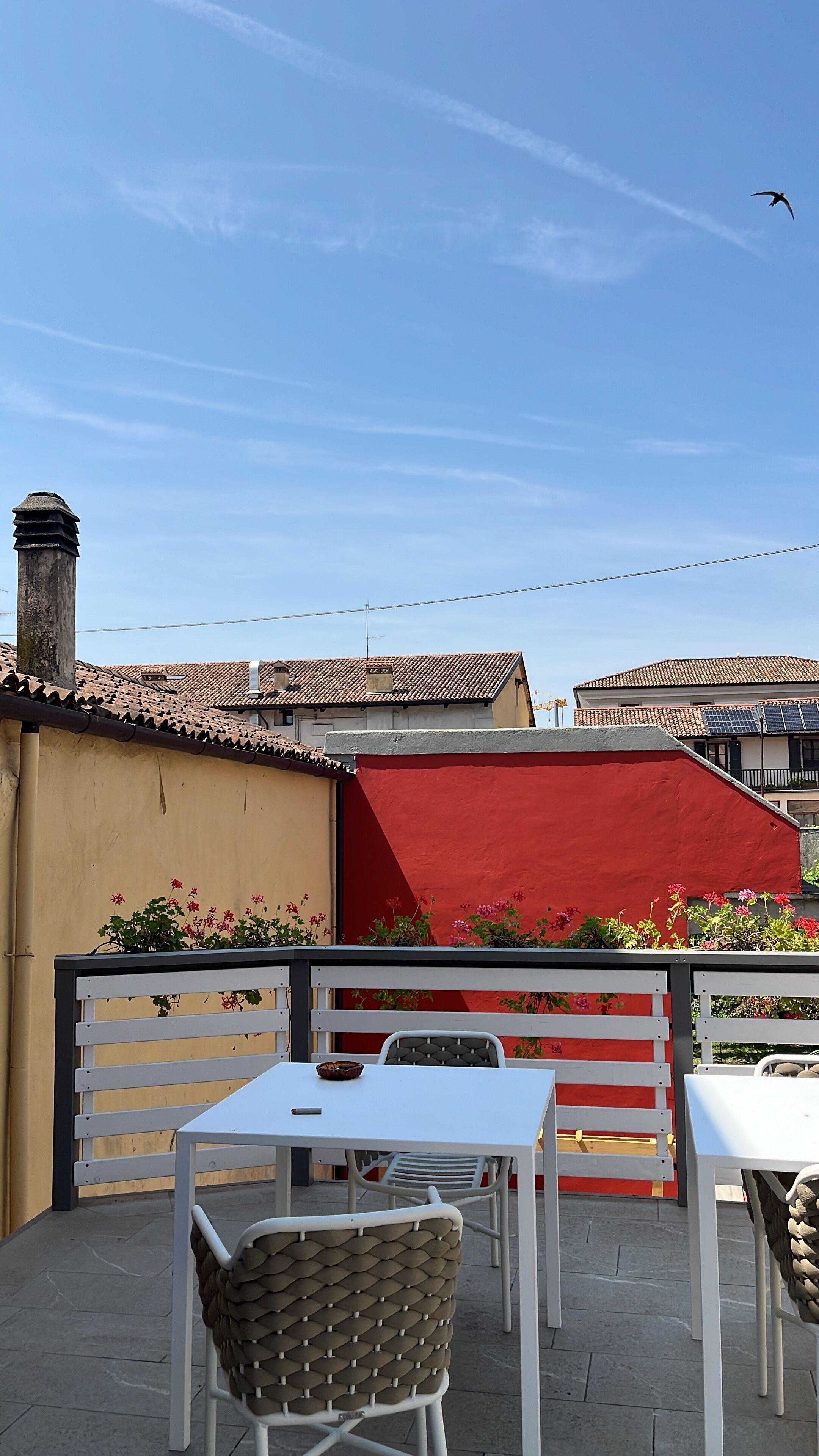An outdoor patio with white tables and chairs, a red awning, and a view of the sky with a bird flying.