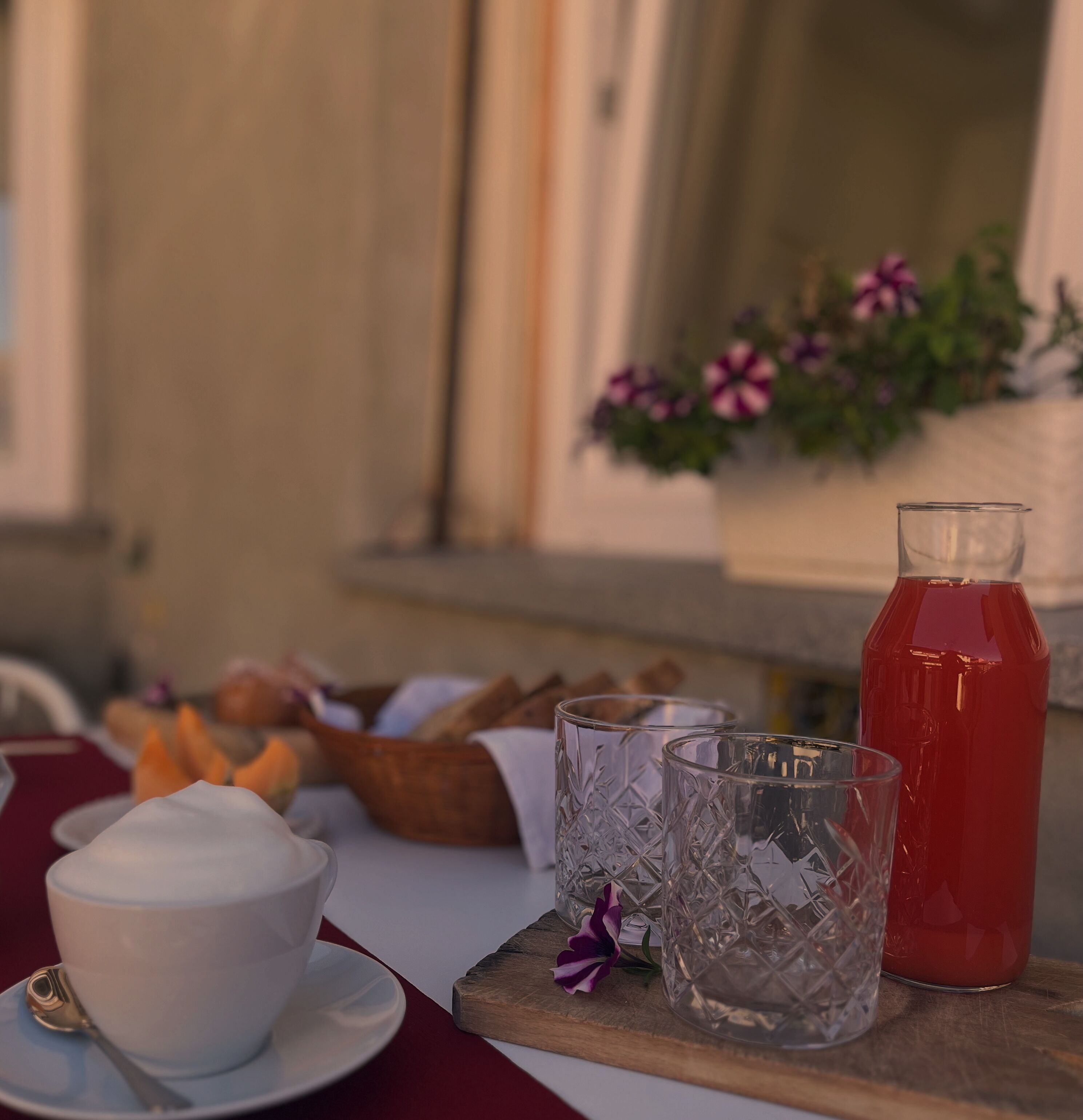 Una mesa con una taza blanca, un vaso, una botella roja y algunos alimentos.