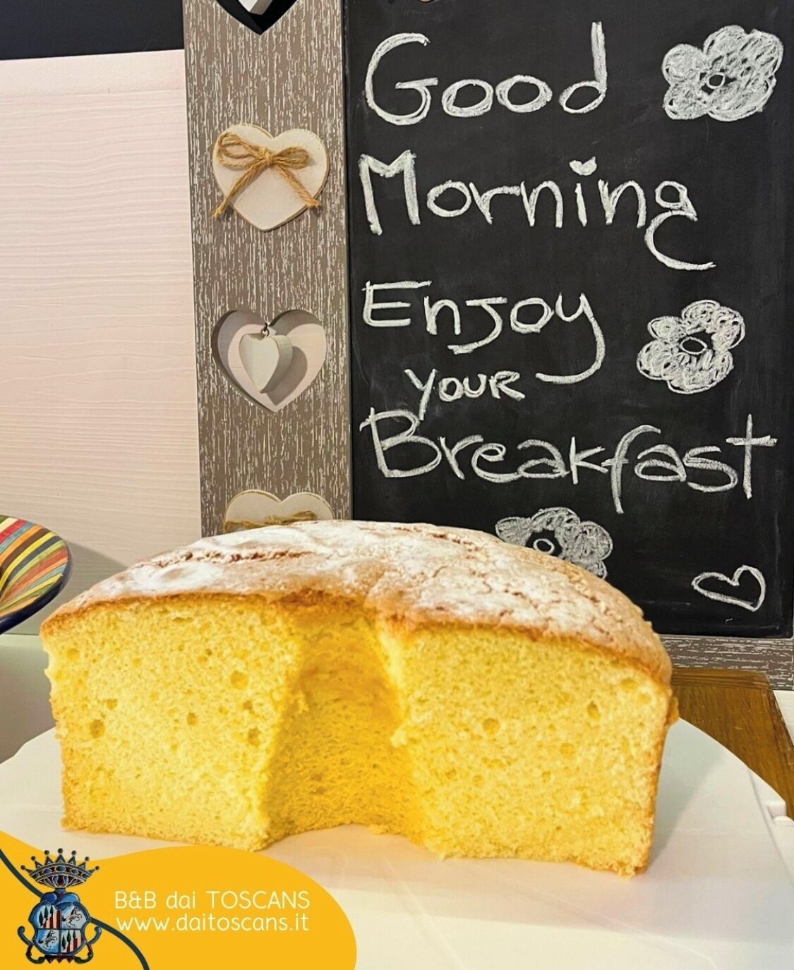 A slice of cake on a plate with a chalkboard in the background that says "Good Morning Enjoy your Breakfast."