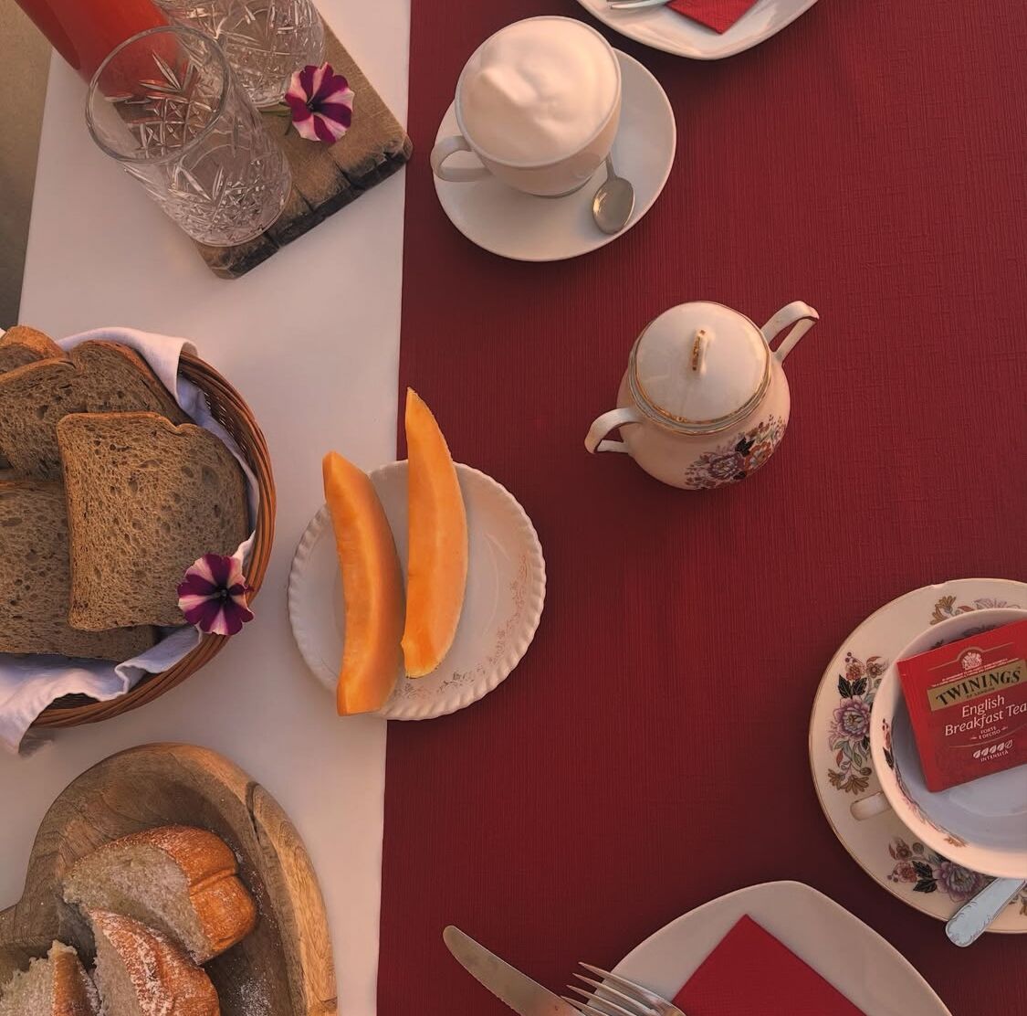Una mesa servida con pan, fruta, una tetera y una bandeja para el desayuno.