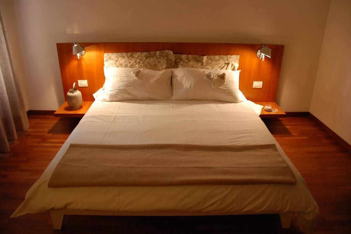 Ein großes Bett mit Holz-Kopfstück, zwei Nachttische und ein Beistelltisch mit Lampe.