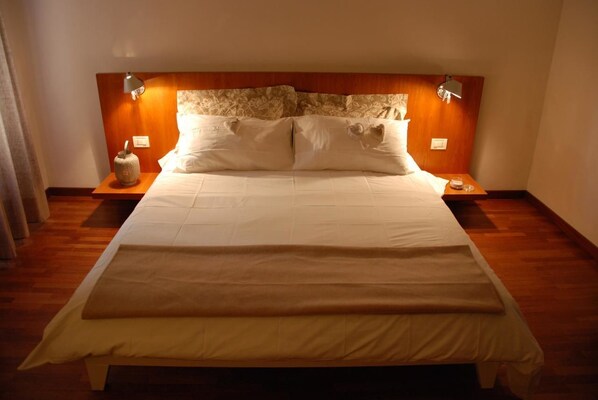 Ein großes Bett mit Holz-Kopfstück, zwei Nachttische und ein Beistelltisch mit Lampe.