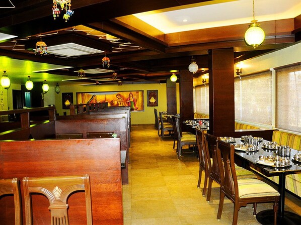 A restaurant with wooden booths and tables, a mural on the wall, and hanging light fixtures. - Hotel Ashray (Ujjain)