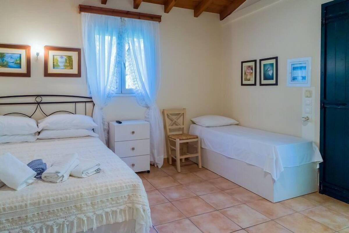 A bedroom with two beds, a chair, and a window with curtains.
