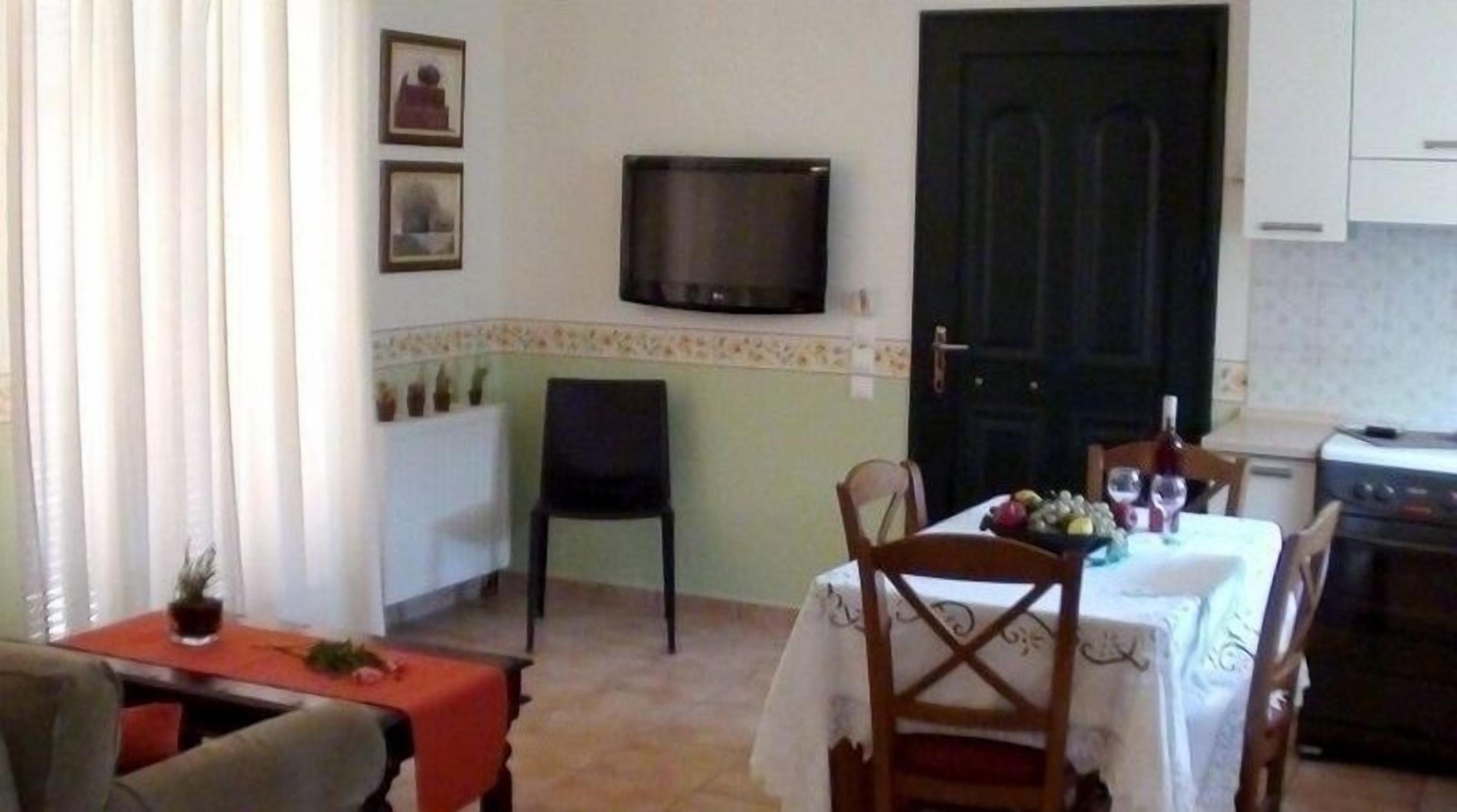 Zona pranzo con tavolo apparecchiato per due, televisore a parete e angolo cottura con piano cottura e pensili.