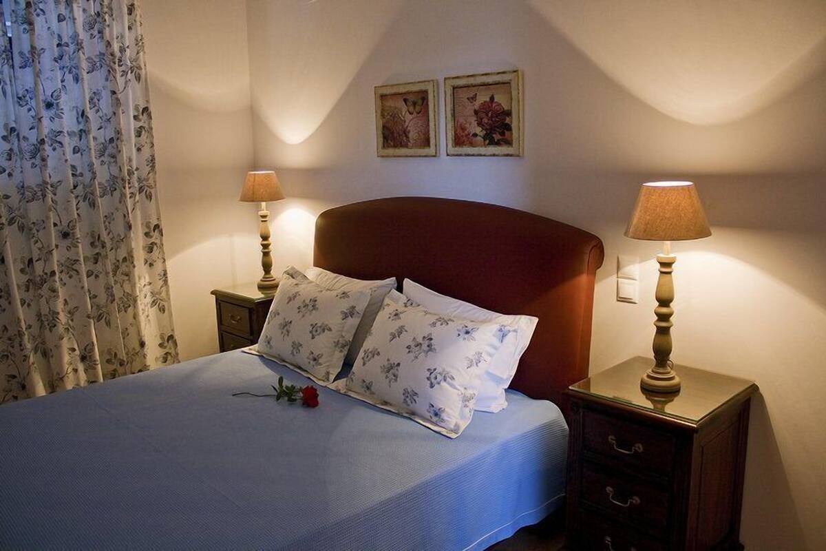 A neatly made bed with floral bedding, two bedside lamps, and a red headboard.