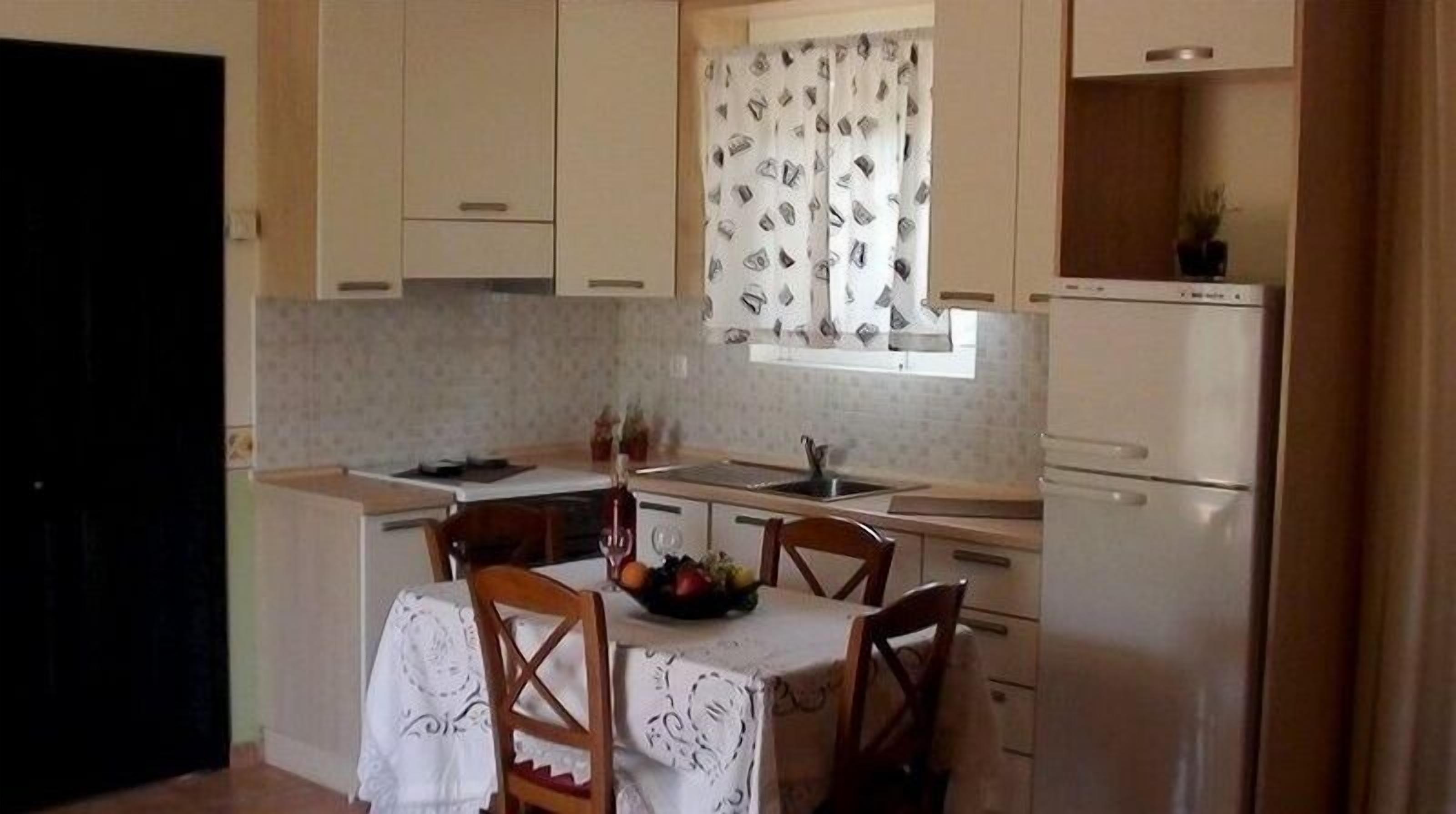 A compact kitchen with a dining table, chairs, a refrigerator, and a window with patterned curtains.