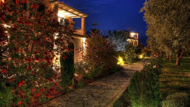A well-lit pathway leading to a building with a balcony and a stone facade. - Anthias Garden (Lefkada)
