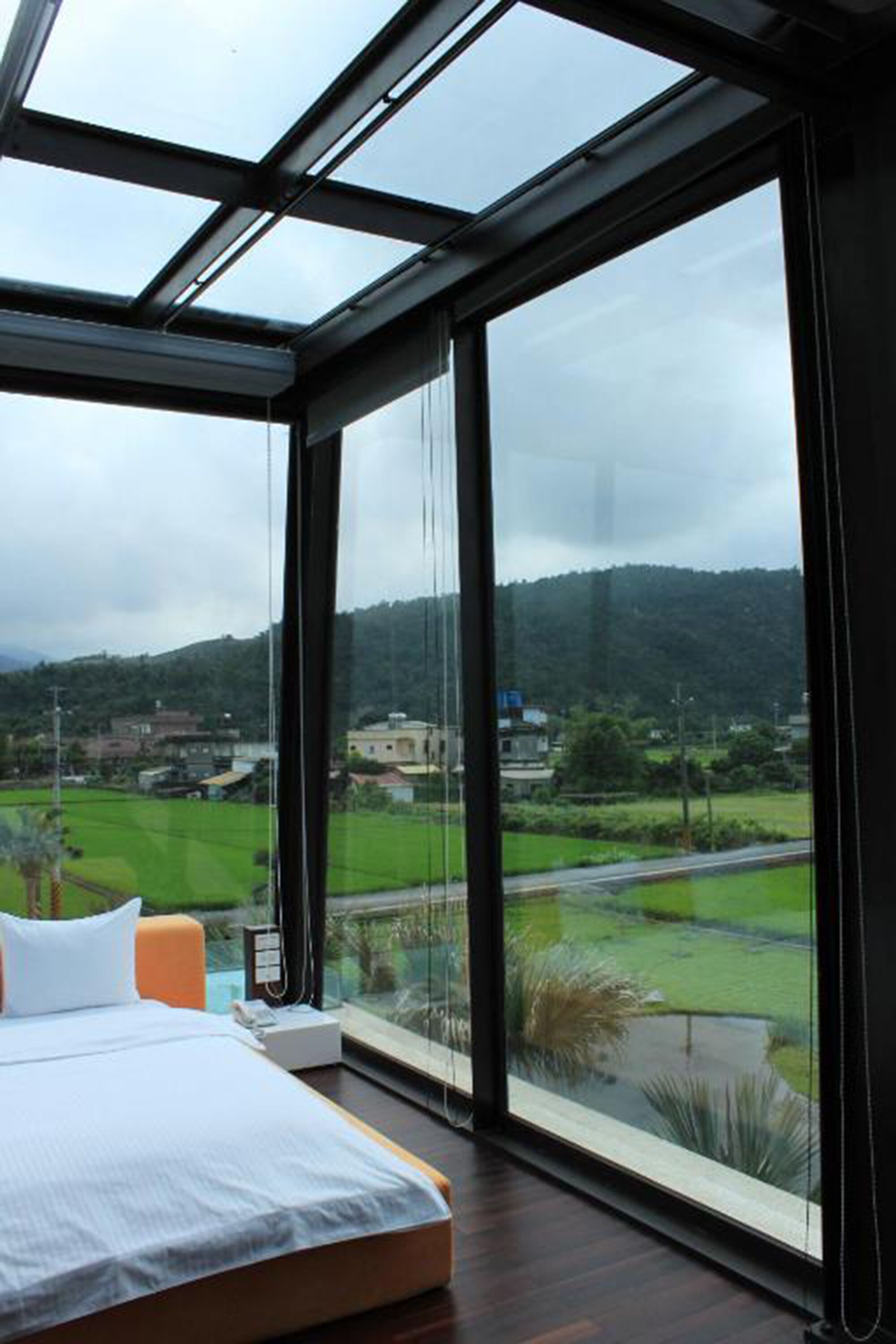 A bedroom with a large window offering a view of a green landscape and distant buildings.