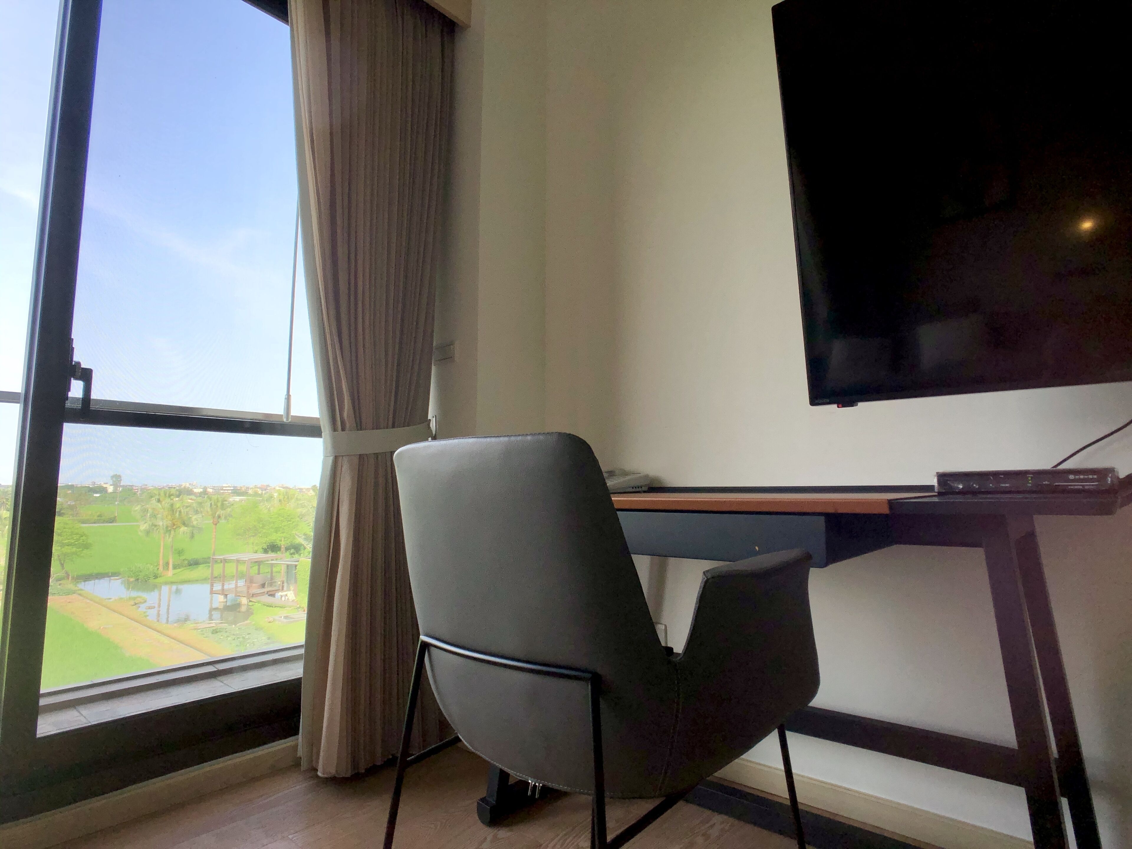 A room with a large window, a desk with a flat-screen TV, and a chair.