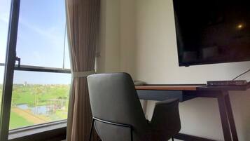 A room with a large window, a desk with a flat-screen TV, and a chair.