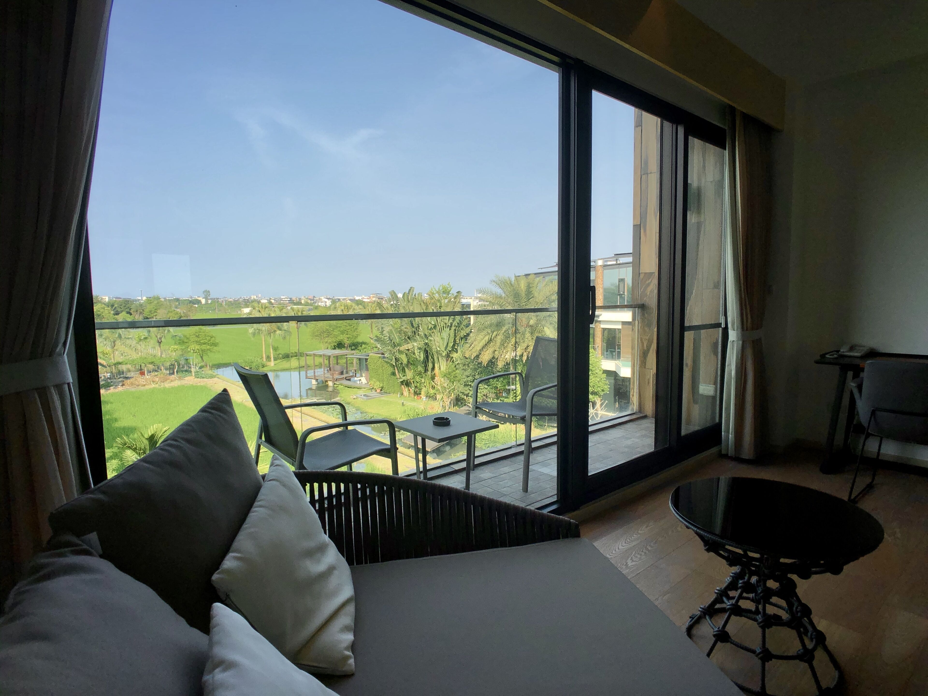 A hotel room with a large balcony, a bed, a table, and a chair.