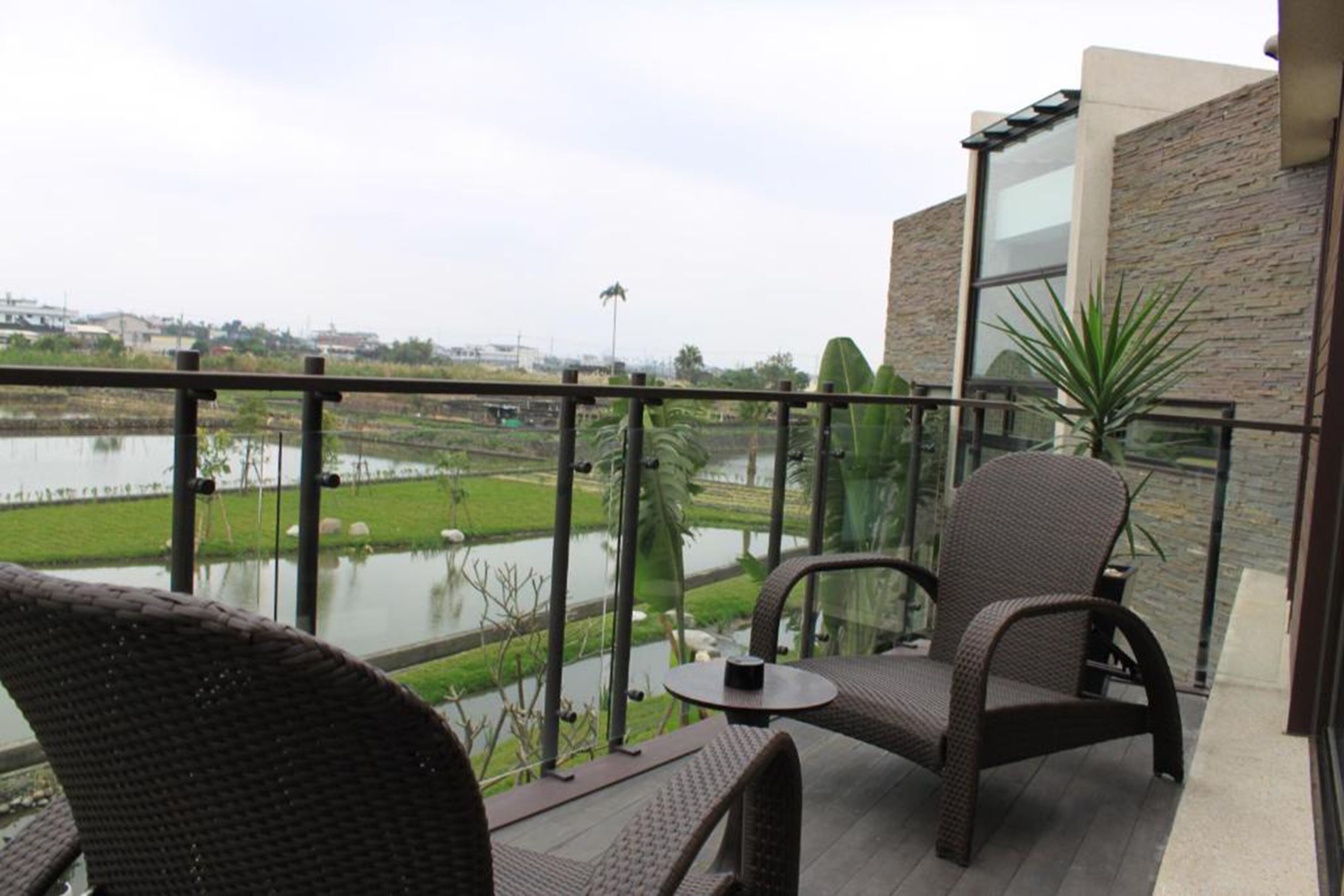 A balcony with wicker furniture, a view of a water body, and a modern building with stone and glass elements.