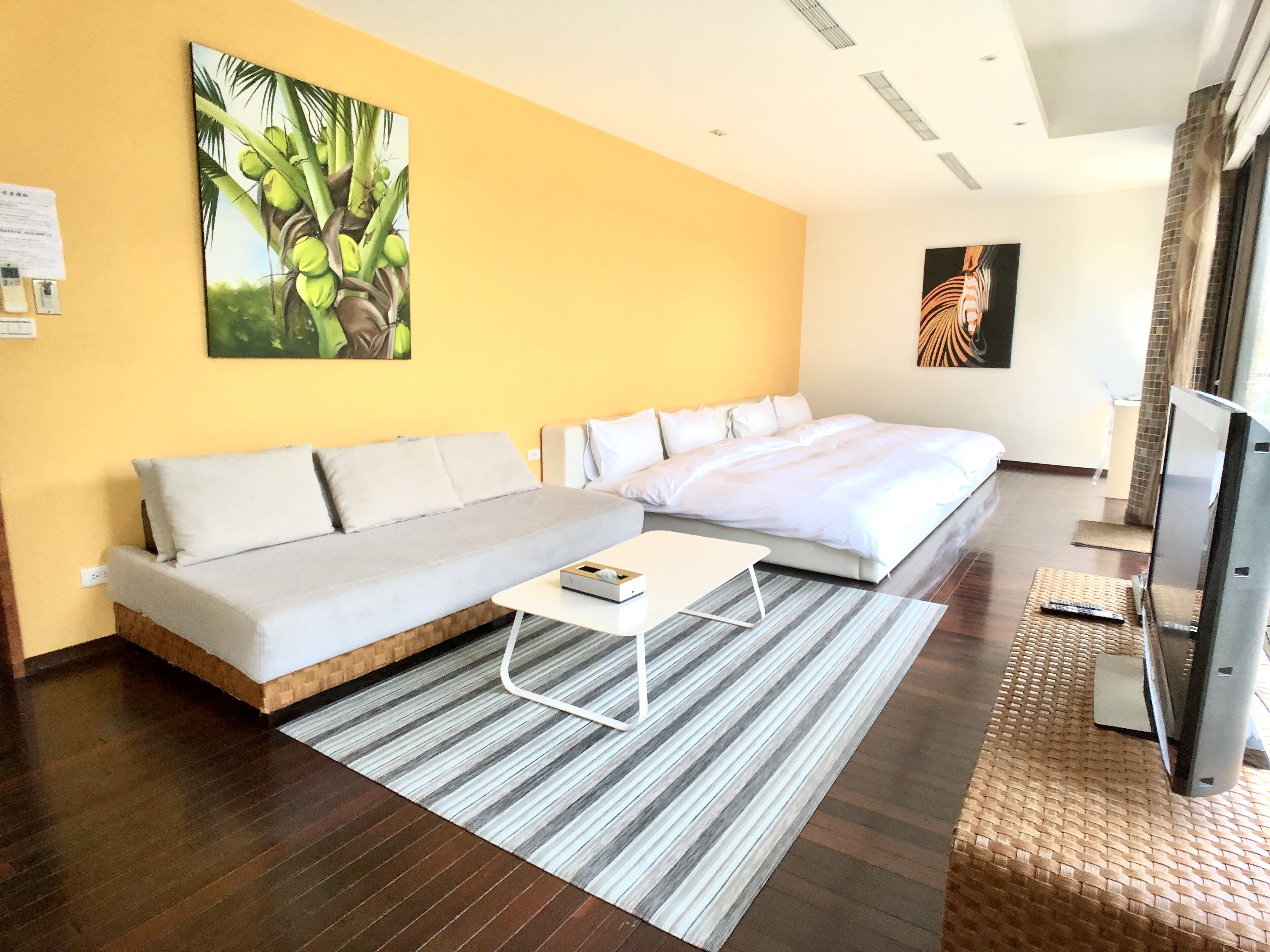 A modern hotel room with a large bed, a sofa, a coffee table, and artwork on the walls.