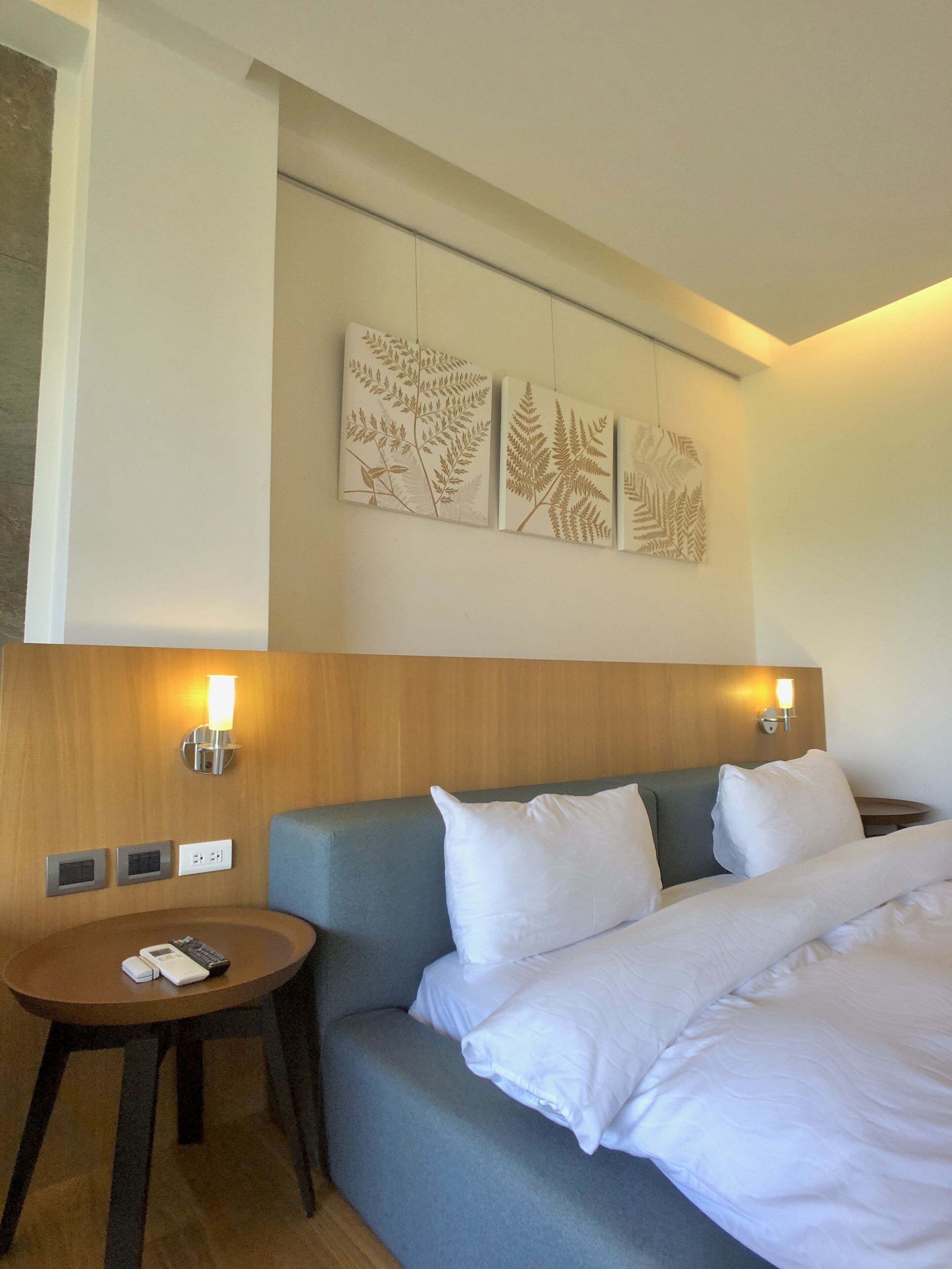 Una habitación de hotel con una cama, una mesa redonda con lámpara y obras de arte colgadas en la pared.