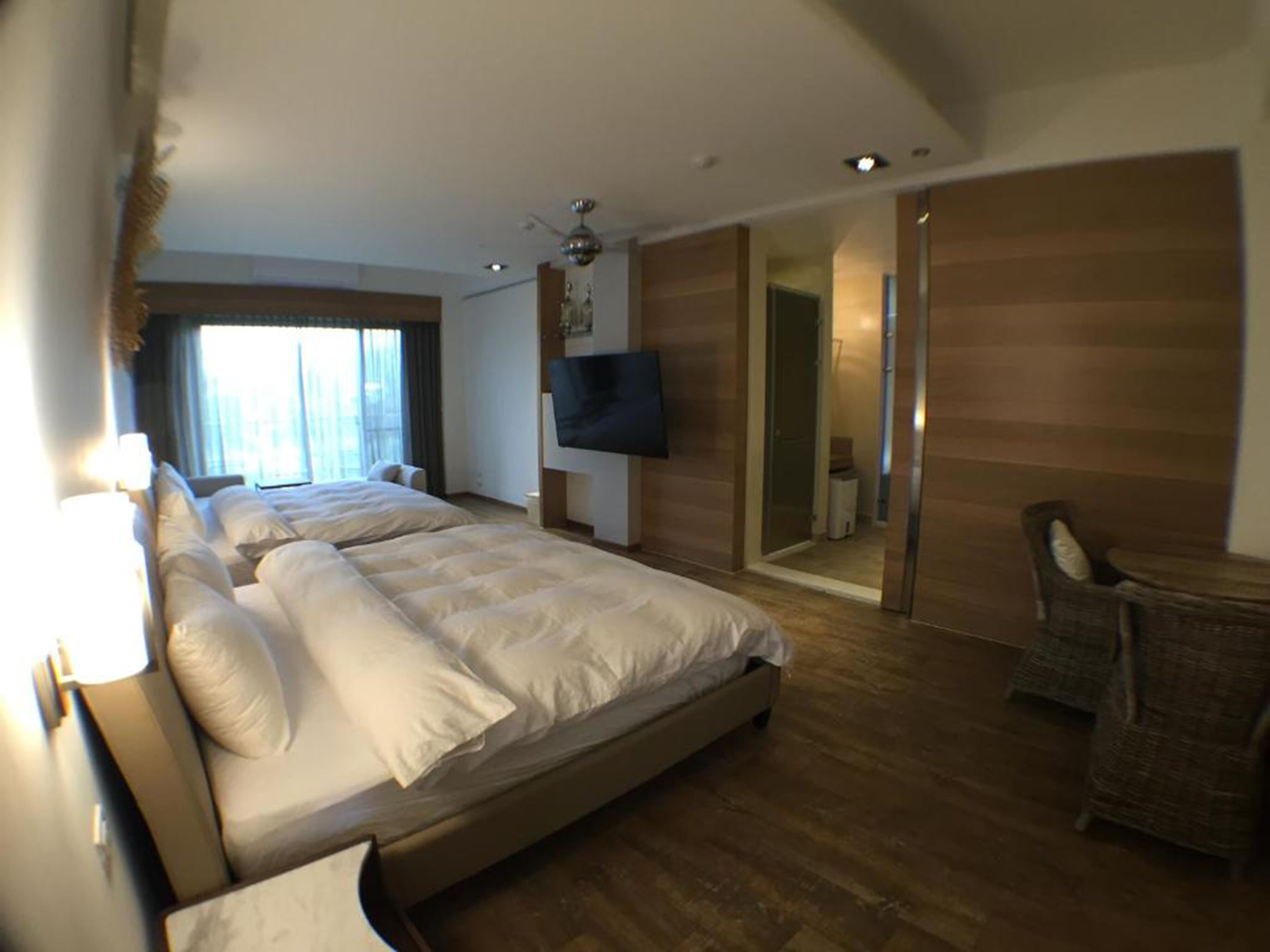 Una habitación de hotel moderna con una cama grande, un televisor montado en la pared y una zona de estar con una silla y una mesita.