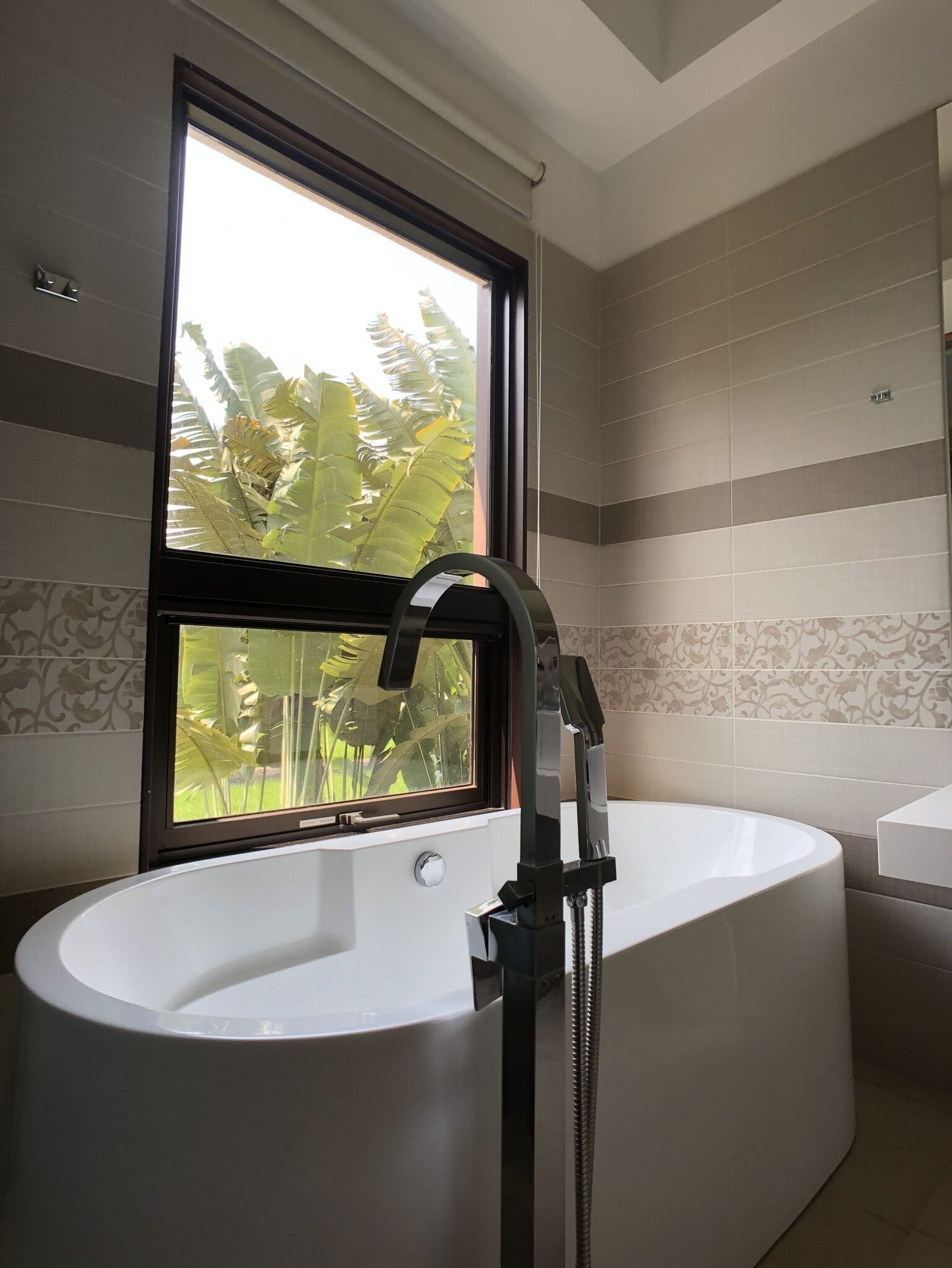 Un bagno moderno con una vasca freestanding, una finestra vista verde e piastrelle decorate alle pareti.
