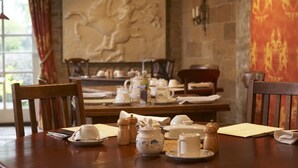 A dining table set with tea service, chairs, and a stone wall with a mural. - The Cornmill Stable Cottages (York)