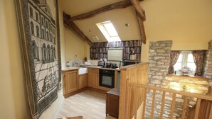 A cozy kitchen with wooden cabinets, a stone wall, and a large window. - The Cornmill Stable Cottages (York)
