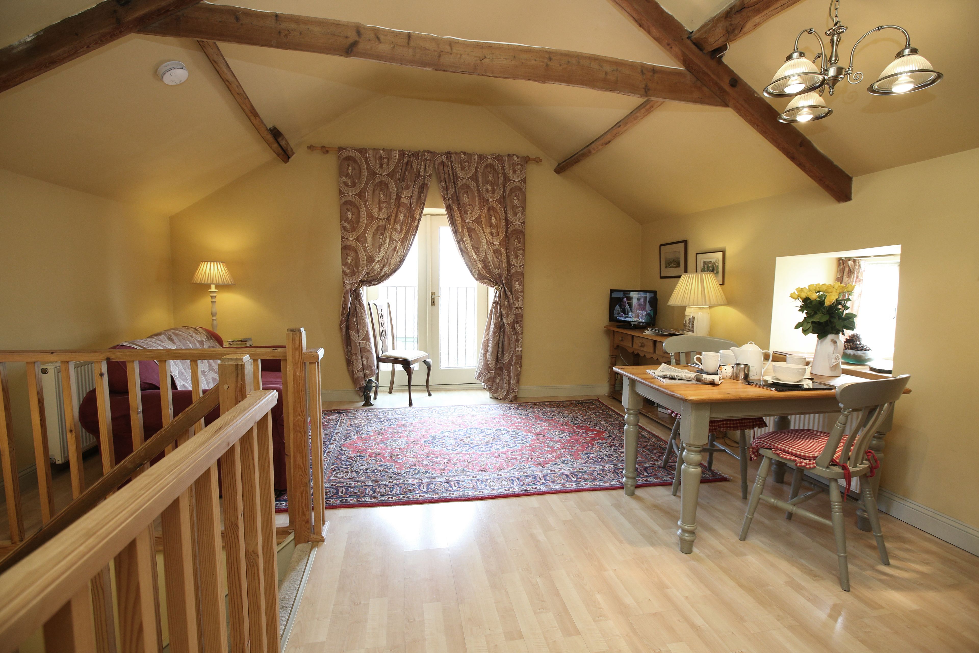 A cozy room with a wooden ceiling, a dining table with chairs, a TV, and a window with curtains.
